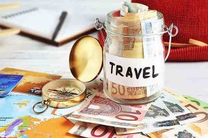 Travel money savings in a glass jar with compass, map and hat.